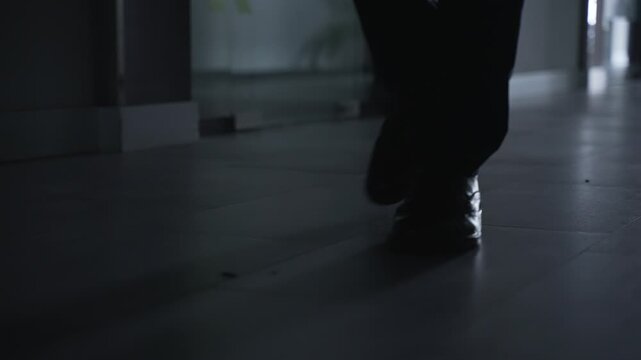 Closeup silhouette of businessman legs walking along dark modern office hallway to business meeting in formal shoes and suit. Low section view male employee footsteps move through corporate center.
