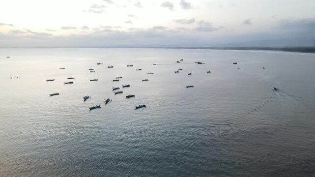 An aerial view of a fleet of small fishing boats on a calm sea at dusk, with a gentle coastline visible in the distance, raw file, log file