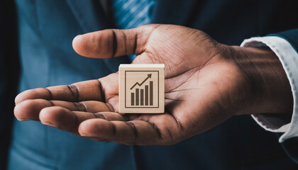 Businessman in a suit holding a small wooden block with a rising bar graph icon symbolizing growth.
