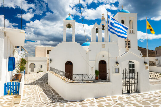 View of church with greek national flag and greek orthodox flag flying on a post outside in the whitewashed sugar cube village of  Marpisssa on Paros