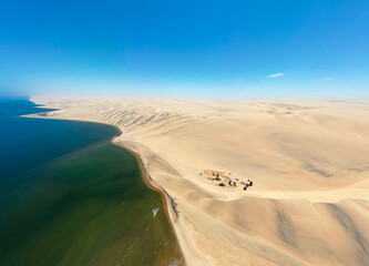 Southern coast of Angola in Iona National Park. The coast has massive dunes. The aerial images show a campsite with vehicles. 