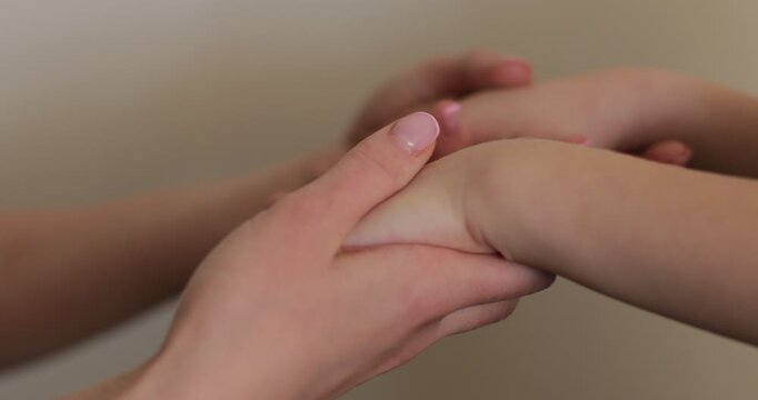 Close up of a woman's hands with a gold wedding ring catching a child's hands and gently rubbing them. Mother and child.
