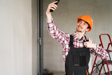Builder, foreman, repairman wearing tool belt hard hat and overalls at construction site making point of view photo showing thumb up, like gesture. Banner.