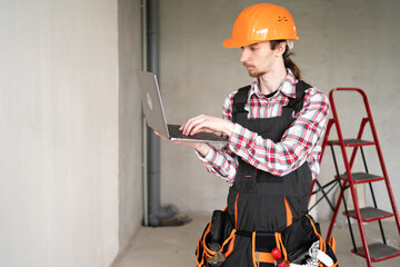 Portrait of young builder, foreman or repairman in orange helmet with laptop
