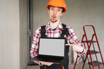 Mock-up. Construction Worker in Hard Hat Pointing At Laptop With Blank Screen Demonstrating Website