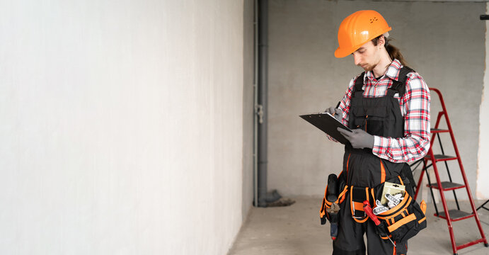 Repairman with a tool belt writing a document in new apartment on wall background. Banner - Powered by Adobe