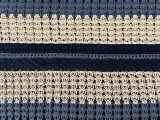 Close up of knitted fabric scarf in stripes pattern, in dark blue, blue, and white color. Suitable for scarf, shawl, table runner, or quilt. Yellow sweater. Seamless background texture