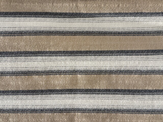 Close up of knitted fabric scarf in stripes pattern, in black, brown, and white color. Suitable for scarf, shawl, table runner, or quilt. Yellow sweater. Seamless background texture