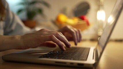 Close-up of a woman's hands typing on a laptop keyboard in a cozy, warmly lit room at night, illustrating the concept of remote work, studying, or late-night freelance projects