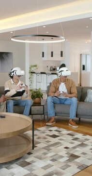 Vertical video: Diverse male pals starting VR game on sofa wearing white headsets with controllers