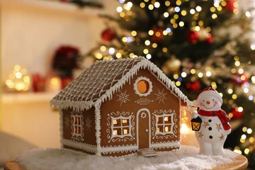 Fotobehang Beren Beautiful gingerbread house, snowman figure and artificial snow on table against blurred lights indoors, closeup. Christmas atmosphere  © New Africa