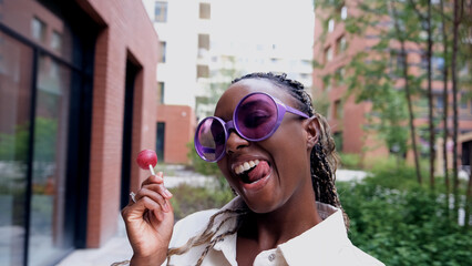 A beautiful woman poses for a smartphone selfie, holding a sweet lollipop.