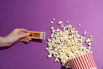 Woman with movie ticket and tasty popcorn on violet background, top view