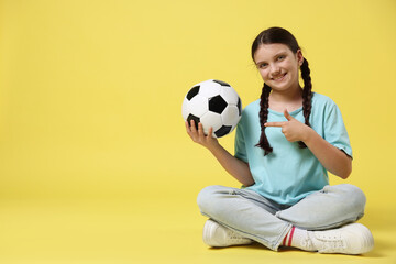 Cute girl with soccer ball on yellow background, space for text