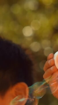 Vertical video: Sunlight warming girl dipping wand then blowing bubble for fun in yard, copy space