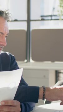 Vertical video: Bringing chart close, man scanning data and typing laptop at desk for review