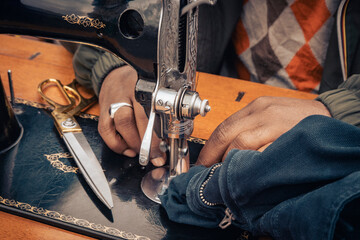 Closeup of hands sewing fabric with a vintage sewing machine and scissors on a wooden table © Lomb