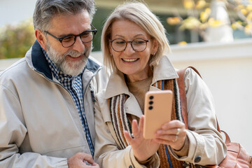 Smiling senior couple looking at a smartphone together while walking outdoors on a sunny day.