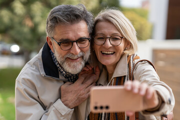 Smiling senior couple taking a selfie together outdoors, enjoying a happy moment and embracing warmly