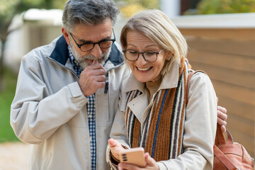 Smiling senior couple looking at a smartphone together while walking outdoors on a sunny day.