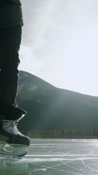 Vertical video: Gliding skater in dark pants balancing after hockey skates contacting mountain ice