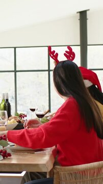 Vertical video: Hearing distant voice, two women passing plates and turning at home table in hats