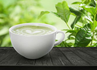 Matcha latte in cup on wooden table against green leaves. Space for text