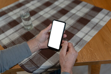Close-up of an older man using a smartphone at a table with a checkered cloth, focusing on his hands and the device