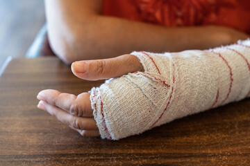 Close-up of an injured hand wrapped in a medical bandage resting on a wooden table.