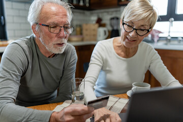 Senior couple using a laptop together at the kitchen table, focused on browsing or managing online tasks
