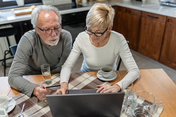 Senior couple using a laptop together at the kitchen table, focused on browsing or managing online tasks