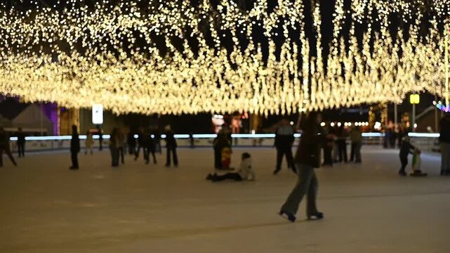 Night ice rink with skaters under glowing festive lights, creating a magical winter holiday atmosphere.