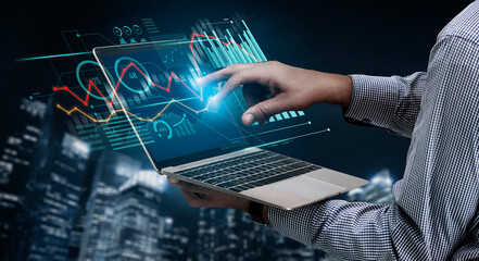 A business professional uses a laptop to analyze data, interacting with holographic graphs and charts against a modern city skyline, showcasing technology and analytics in action. Scalp