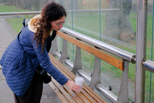 Woman standing at bus stop drinking takeaway coffee