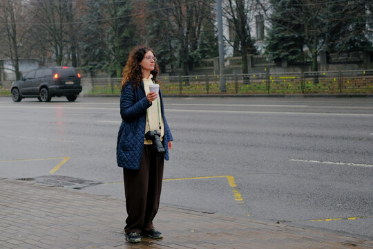 Woman waiting for transport at a bus stop with takeaway coffee