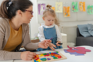 Fototapeta premium Caregiver and young girl engaging in a learning activity with colorful wooden blocks in a bright preschool classroom