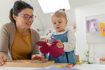 Mother and young daughter enjoy a creative crafting activity together, cutting and gluing colorful...