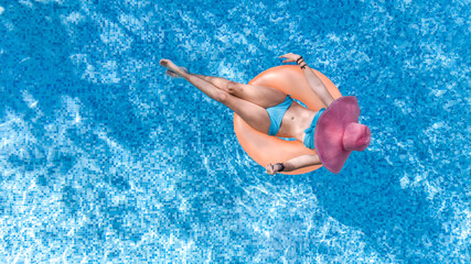 Aerial drone view of beautiful woman in hat relaxing in swimming pool, young girl in bikini swims on inflatable ring donut and has fun in blue pool water, tropical vacation on holiday resort