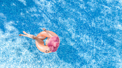 Aerial drone view of beautiful woman in hat relaxing in swimming pool, young girl in bikini swims on inflatable ring donut and has fun in blue pool water, tropical vacation on holiday resort