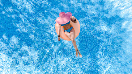 Aerial drone view of beautiful woman in hat relaxing in swimming pool, young girl in bikini swims on inflatable ring donut and has fun in blue pool water, tropical vacation on holiday resort