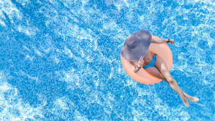 Aerial drone view of beautiful woman in hat relaxing in swimming pool, young girl in bikini swims on inflatable ring donut and has fun in blue pool water, tropical vacation on holiday resort