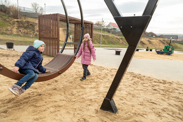 Children having fun on a swing on the playground in public park on autumn day. Happy child enjoy swinging. Active outdoors leisure for child in city