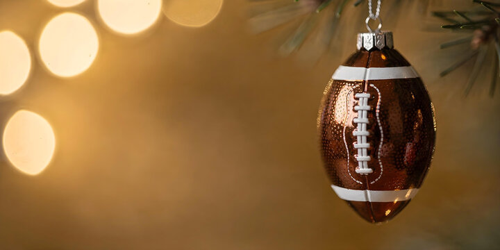 Christmas ornament shaped like a brown football with white lacing, hanging from a spruce branch against a golden background with bokeh lights.
