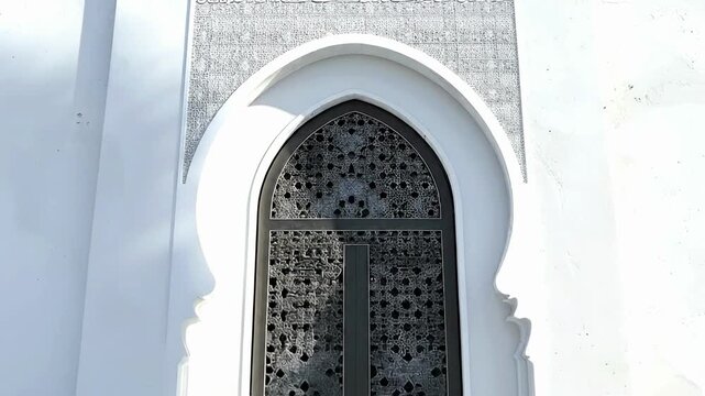 An ornate dark metal grille window within a white horseshoe arch set in a bright white wall with a textured frieze above