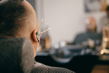 Caucasian male getting groomed at barbershop with cotton swabs, ear waxing