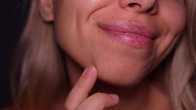 Young blonde woman touching her cheek and showing a cute dimple in a soft close-up on a dark background, highlighting natural beauty and subtle facial features