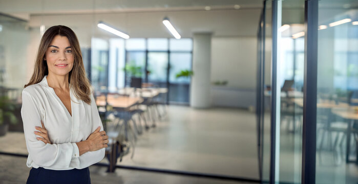 Smiling confident Latin professional mid aged business woman in 40s, corporate leader, happy mature female executive, lady manager standing in office arms crossed looking at camera, portrait. Banner