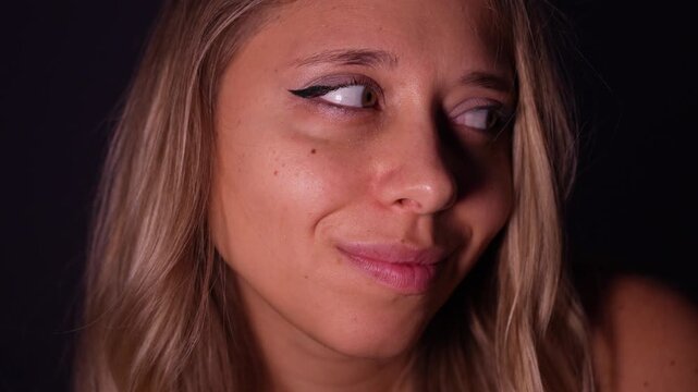 Young blonde woman smirking with a raised brow, giving a playful and flirty look in soft studio lighting on a dark background