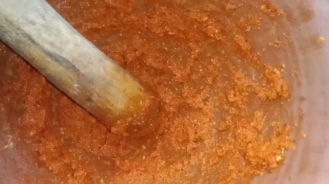 Closeup of red chili paste being ground on a traditional stone mortar and pestle showing rich texture vibrant color and natural spices blending into a smooth aromatic mixture