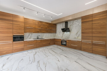 This kitchen features wooden cabinets and marble flooring. It has modern appliances and a large countertop space. The design showcases clean lines and open layout